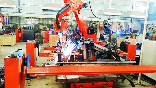 Orange robot welding a part at a welding station, with sparks, inside a factory
